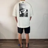 Remera negra de algodón pesado, corte oversize, con un gran estampado en la espalda en blanco y negro que muestra la parte inferior del rostro de una persona con un gorro tejido cubriendo los ojos y un cigarrillo en la boca.