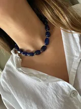 Collar corto compuesto por piedras ovaladas de color azul profundo, intercaladas con pequeñas cuentas plateadas. Está confeccionado en acero quirúrgico e incluye una cadena de alargue para ajustar el largo deseado.