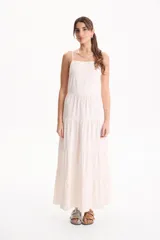 Vestido largo color blanco, confeccionado en lino, con tiras finas regulables, escote recto y falda amplia de corte acampanado con volados escalonados.