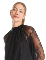 Blusa de encaje negro con cuello halter y mangas largas transparentes. Presenta un diseño elegante con detalles florales en el encaje y cierre con lazo en la espalda.