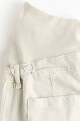 Jean tobillero de denim de algodón con leve stretch, diseño de pierna ancha y corte holgado. Modelo de tiro alto con panel de punto elástico para maternidad y pliegues en las piernas.