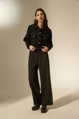 Chaqueta de jean negra con corte holgado, cuello camisero, cierre frontal con botones y detalle de strass y tachas metálicas distribuidas en el frente y mangas.