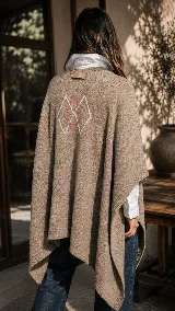Ruana de algodón color beige, de diseño amplio y envolvente, con detalle de bordado artesanal en la espalda que forma rombos en tonos blanco y fucsia.