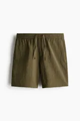 Pantalón corto de tejido texturizado verde militar, con corte relajado, cintura elástica con cordón de ajuste y bolsillos laterales.