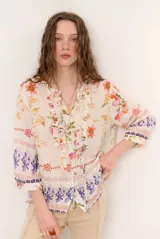 Blusa de manga tres cuartos color beige con estampado floral multicolor, escote en V y detalles de volados frontales junto a la botonadura.