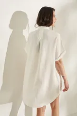 Vestido corto color beige de lino, con moldería amplia, manga corta, cuello mao y cierre frontal con botones dorados.