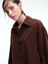 Camisa oversize de lyocell color tostado, con cuello clásico, cierre frontal de botones y mangas largas con puños anchos. Presenta un diseño de corte relajado con caída fluida.