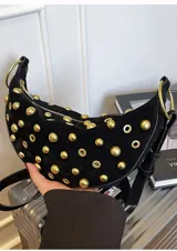 Bolso pequeño de hombro con forma de media luna, color negro, decorado con tachas redondas doradas. Cuenta con una correa ajustable y herrajes dorados.