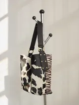 Cartera tipo hobo de cuero azul con textura granulada. Presenta un diseño holgado, con una correa de hombro bicolor que combina azul y rojo, sujeta por argollas metálicas. Incluye una placa metálica pequeña con el logo de la marca en la parte inferior frontal.