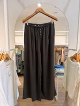 Pantalón gris oscuro de corte amplio y fluido, con cintura elástica fruncida, lazo de ajuste y detalle de botones frontales.