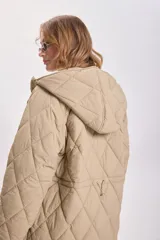 Campera color beige con capucha, cierre frontal con cremallera y broches a presión, bolsillos laterales y diseño acolchado con patrón de rombos.