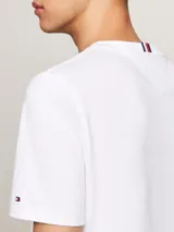 Remera de algodón Tommy Hilfiger, color blanco, con cuello redondo y manga corta. Presenta el logo de la marca bordado en el pecho en tipografía cursiva y la bandera distintiva bordada en la manga.