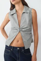 Top sin mangas con cuello camisero, escote en V profundo y detalle fruncido en los laterales. Confeccionado en tejido a rayas.