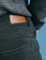 Pantalon denim de cinco bolsillos, corte recto y color negro, con botones y remaches metálicos en tono plata viejo.