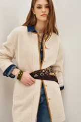 Saco de corte recto confeccionado en tejido tipo boucle color crema, con terminaciones en contraste color marrón y cierre frontal con botones metálicos.