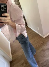 Camisa de algodón color rosado, de corte holgado, con cuello clásico, cierre frontal con botones y mangas largas abullonadas con detalles fruncidos.