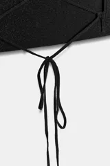 Top negro con escote asimétrico, tirante fino doble en un hombro y detalle de tiras cruzadas con lazada en la espalda.