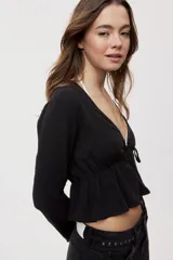 Blusa manga larga de color negro con escote en V profundo y lazo ajustable en el frente, confeccionada en tejido liviano con corte evasé.