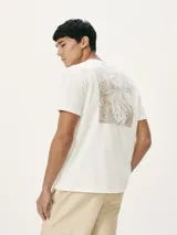 Camiseta blanca de algodón con cuello redondo y mangas cortas. Estampa rectangular con borde negro que contiene la frase "NATURAL ATMOSPHERE" en letras mayúsculas y una imagen de montañas y mar.