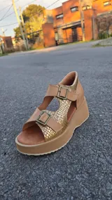 Sandalias de cuero color tostado con plataforma y taco chino, tiras frontales y laterales con hebillas ajustables y detalles en tono dorado texturizado.