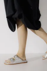 Sandalias de cuero color negro con dos tiras anchas sobre el empeine, cada una con hebillas metálicas ajustables y detalles de tachas plateadas. La suela es de cuero con un borde de color madera.