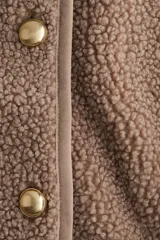 Chaqueta de sherpa suave con cuello redondo, corte holgado y cierre frontal con botones metálicos. Presenta ribetes de cinta en los bordes.