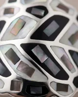 Anillo de acero de diseño amplio con patrón geométrico esmaltado en tonos blancos, negros y grises, y detalles de nácar.