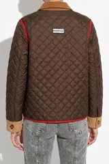 Campera capitoneada color marrón con detalles en pana color tostado en cuello, puños y solapas de bolsillos. Presenta ribetes en color rojo, cierre frontal con botones y diseño acolchado.