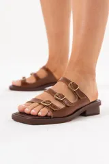 Sandalia de cuero marrón con diseño de tres tiras con hebillas metálicas doradas regulables y punta cuadrada.