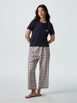 Pijama compuesto por una remera de manga corta en color azul marino con un pequeño bordado en el pecho y un pantalón largo de corte recto con estampado de cuadros y estrellas pequeñas.