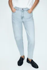 Jeans tipo mom fit de tiro alto color blanco, con diseño de cinco bolsillos, cierre frontal con cremallera y botón, y corte tobillero.