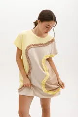 Vestido corto de algodón, con bloques de color en tonos pastel (amarillo claro, beige y rosado pálido) unidos por volados fruncidos en tonos marrón claro y amarillo. Presenta cuello redondo y mangas cortas.