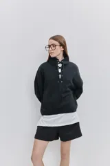Buzo de algodón negro con calce relajado, cuello alto con cordones cruzados y ojales metálicos, bolsillos laterales y puños y ruedo elásticos.