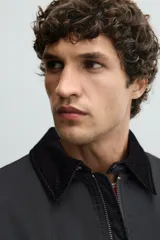 Parka de corte relajado en color negro, confeccionada en tejido de algodón con interior ligeramente acolchado. Presenta cuello de solapa en pana, cierre frontal con cremallera y bolsillos delanteros tipo plastrón con solapa y botones a presión.