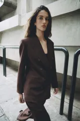 Blazer de corte sastre con cuello solapa, manga larga y hombreras marcadas. Presenta un diseño cruzado con cierre frontal de botones, bolsillos delanteros de vivo y abertura posterior en el bajo.