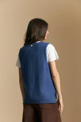 Chaleco tejido color azul, con escote en V, cierre frontal con botones y diseño de líneas verticales en relieve. Presenta terminaciones acanaladas en el ruedo y un borde ondulado en el escote.