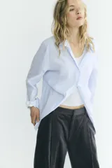 Camisa oversize de algodón con estampado de rayas finas, cuello solapa, escote en pico y manga larga con puños abotonados. Presenta un diseño con pliegues laterales y cierre frontal con botones.