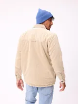 Sobrecamisa de pana color beige, con cierre frontal de botones a presión, dos bolsillos frontales con solapa y bolsillos laterales. Presenta cuello clásico y diseño acolchado con forro interior.