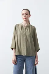 Camisa de color celeste claro con silueta relajada y mangas largas. Presenta un cuello redondo con pequeña abertura frontal y botones, además de un delicado trabajo de tablas en los hombros que aporta textura al diseño.