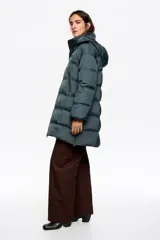 Campera tipo plumífero de largo medio con silueta en línea A, confeccionada en tejido técnico brillante. Presenta cierre frontal con cremallera, cuello subido con capucha desmontable, mangas largas con puños interiores de pelo sintético y bolsillos laterales con cremallera.