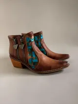 Botas cortas de cuero marrón terracota con diseño pintado a mano en la parte frontal en tonos turquesa y dorado. Cuentan con taco cuadrado de madera, doble cierre lateral con tiradores metálicos personalizados y punta fina.