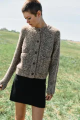 Chaqueta de punto de cuello redondo y manga larga, con textura jaspeada en tonos tierra y azul. Presenta cierre frontal con botones oscuros y dos bolsillos de plastrón en el delantero.