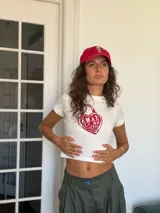 Remera tipo baby tee de corte ajustado y largo cropped, color blanco con estampa frontal en forma de corazón rojo que incluye la frase 'Amar es no poseer'.