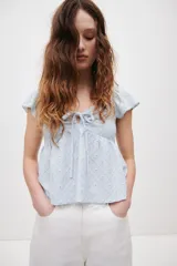 Blusa corta celeste de punto pointelle con textura, escote corazón, mangas cortas con vuelo y cordón de ajuste en el centro del busto.