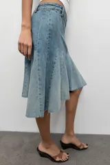 Falda de jean de tiro medio con efecto lavado, diseño con godets y costuras marcadas. Presenta un bajo asimétrico con acabado desflecado, cierre frontal con cremallera y botón metálico.