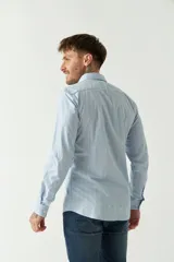 Camisa de hombre de corte slim fit, confeccionada en algodón con diseño de rayas verticales finas en tonos claros. Presenta cuello clásico, cierre frontal con botones y logo bordado en el pecho.