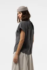 Camisa gris de corte relajado, con escote en V y lazo largo incorporado en el cuello. Mangas cortas con vuelta y frunce sutil en los hombros.