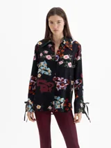 Camisa de seda color blanco con estampado floral y de dragones en tonos rojos, azules y verdes. Tiene cuello clásico, mangas largas con puños ajustables y botones forrados.