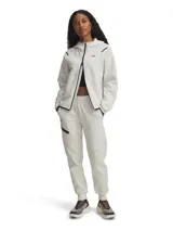 Jogger deportivo Under Armour de tejido doble punto, color beige claro. Presenta cintura elástica con cordón interno, bolsillos laterales abiertos y un bolsillo cargo con cremallera en el muslo derecho. Diseño de corte ajustado en las piernas con puños elásticos en los tobillos.