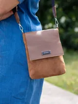 Bandolera Terrano de diseño compacto, confeccionada en una combinación de cuero sintético liso en la solapa y textura tipo gamuza en el cuerpo principal. Presenta una placa metálica con el logo de la marca en el frente, correa regulable y herrajes plateados.